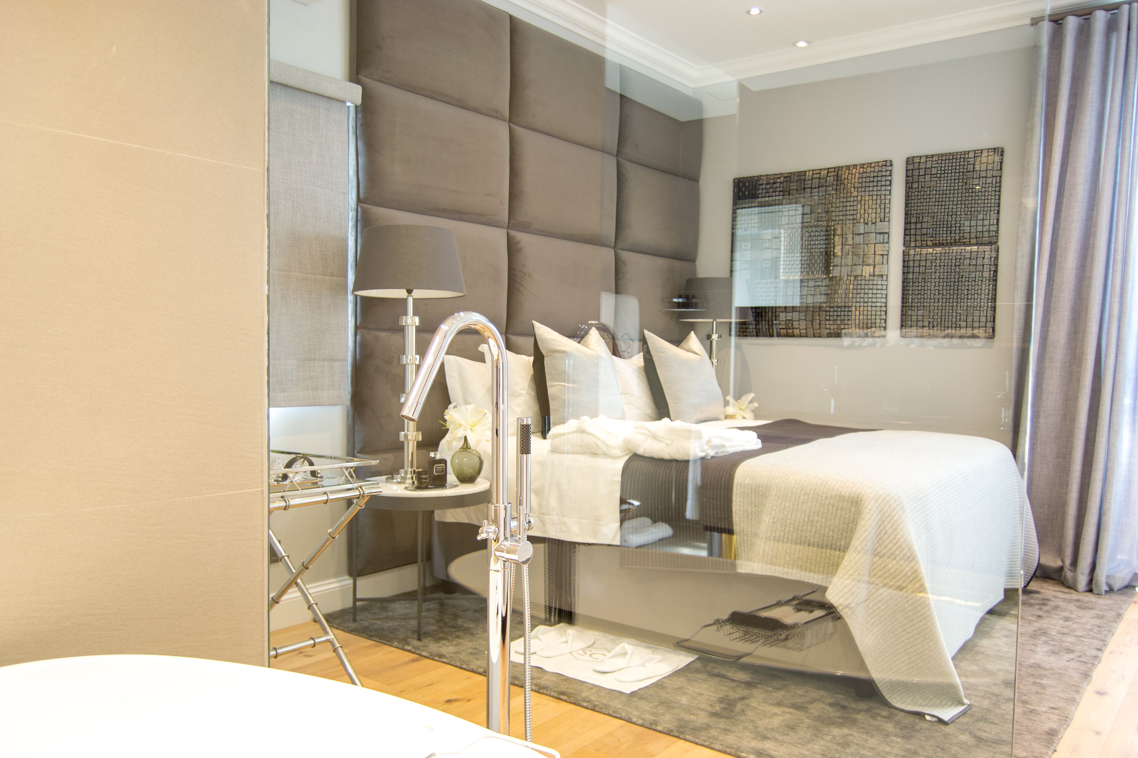 A modern hotel room with a large bed, a glass shower enclosure, and a decorative mirror on the wall.