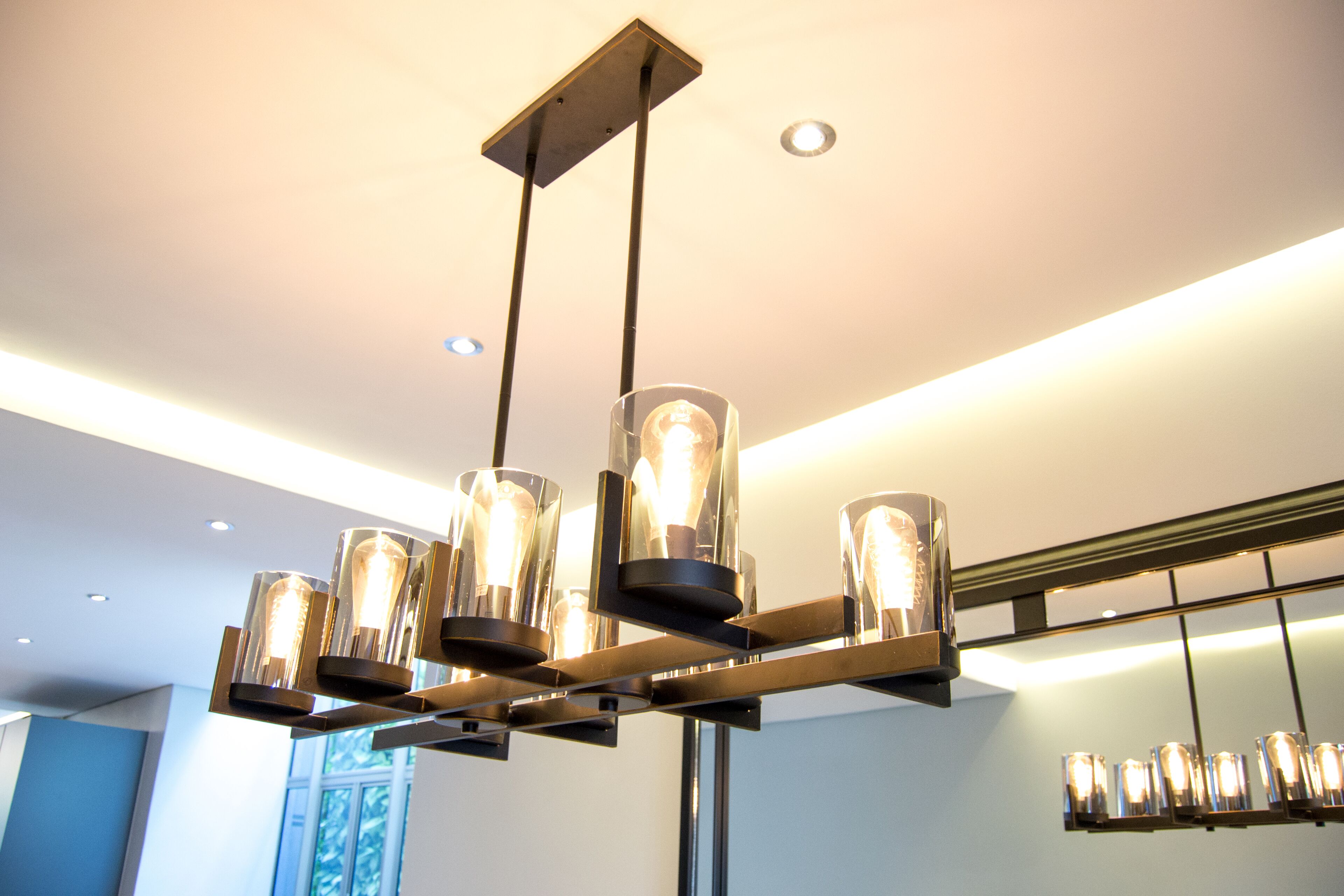 Un lustre moderne doté de plusieurs abat-jour en verre et de lampes apparentes, suspendu à un support métallique.