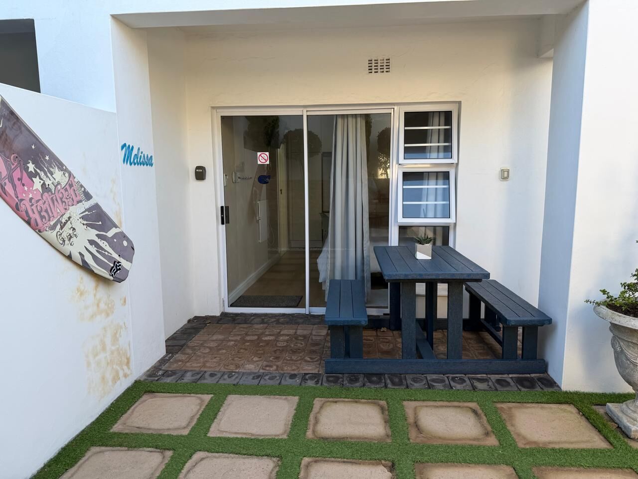 A covered patio area with a sliding glass door, a picnic table, and a potted plant.
