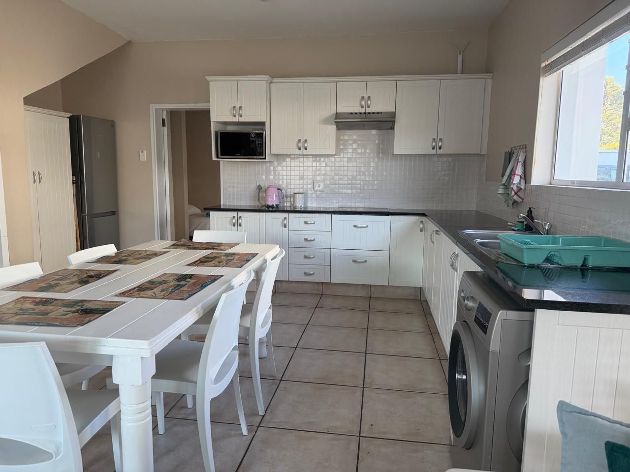 A kitchen with white cabinets, a washing machine, and a dining area with a table and chairs.