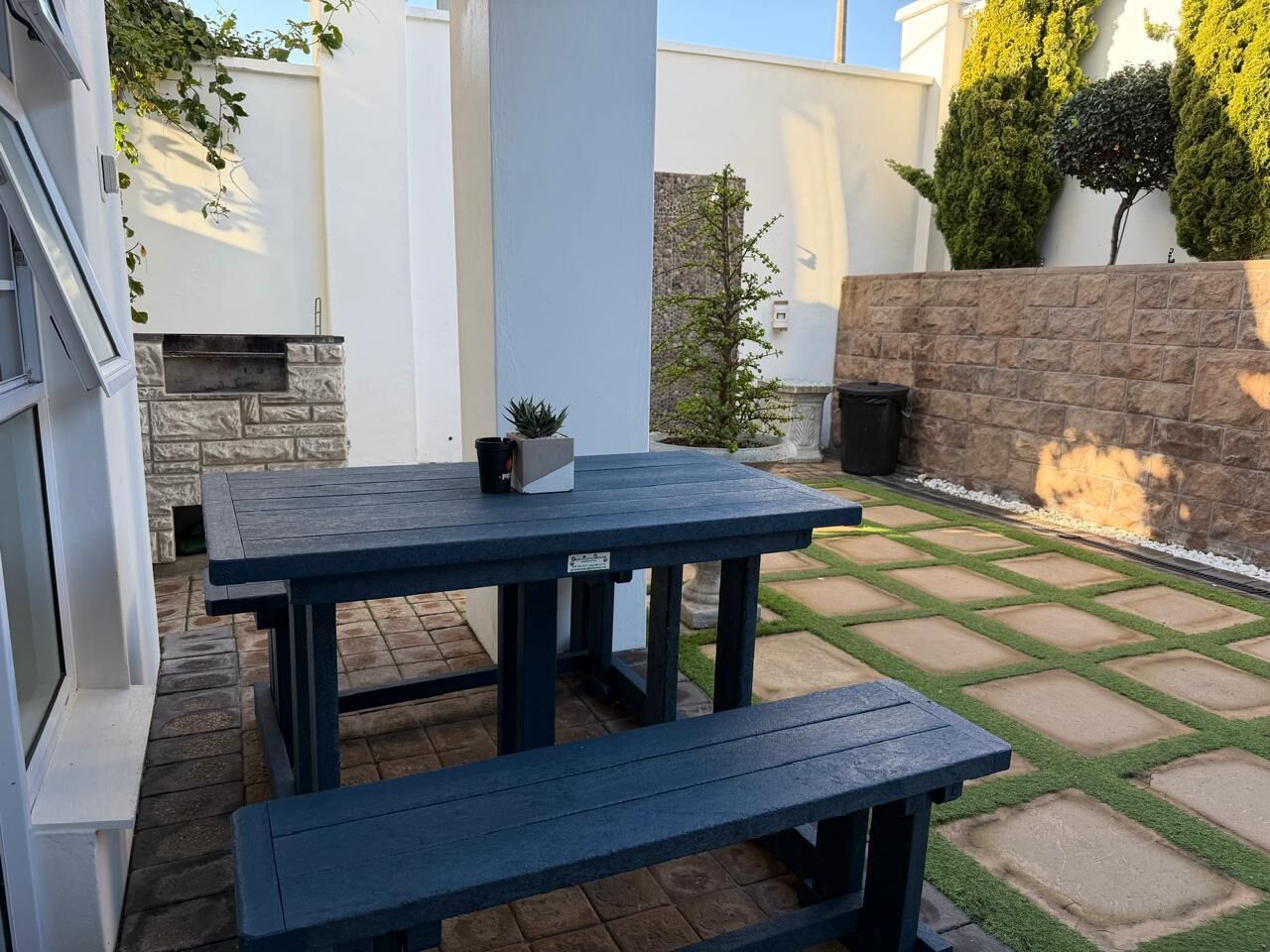 Un patio con una mesa, bancos, un muro de piedra y una pequeña planta en maceta.