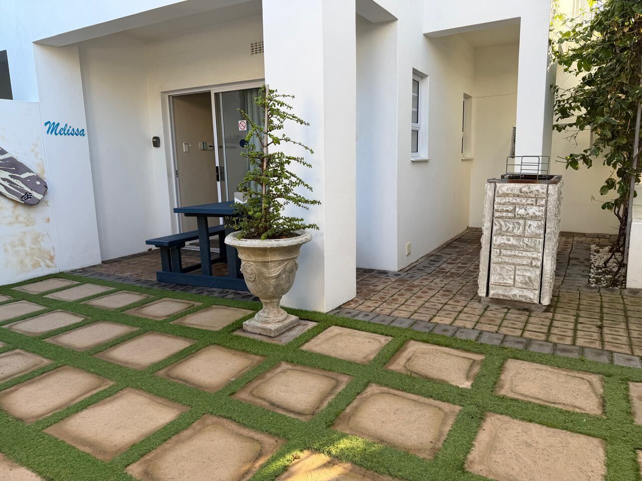 A courtyard with a stone bench, a potted plant, and a stone fireplace.