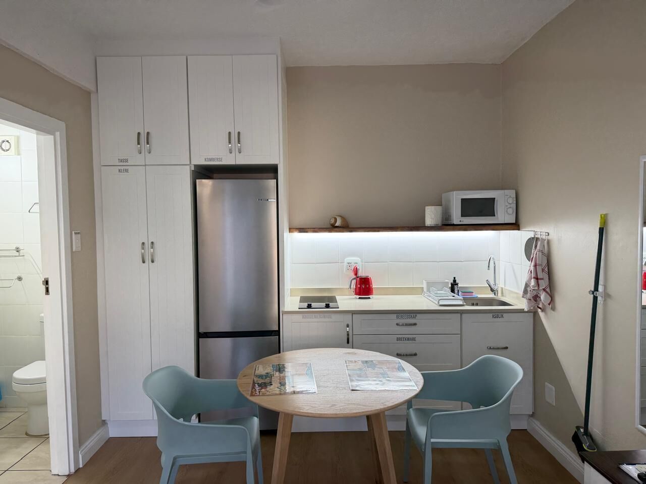 A compact kitchen with a refrigerator, microwave, and a sink. There is a dining table with two chairs.