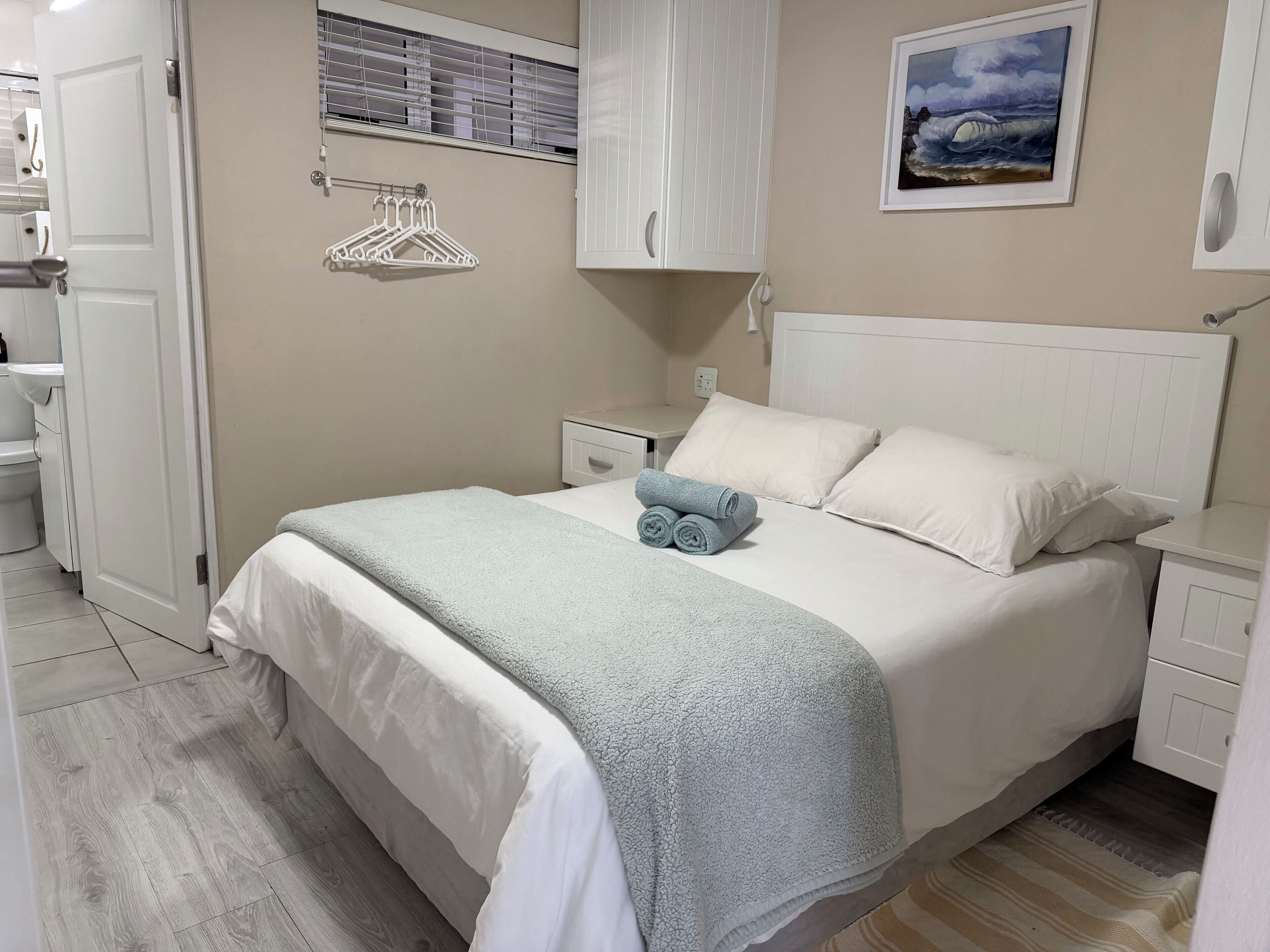 A neatly arranged bedroom with a bed, bedside tables, a wardrobe, and a painting on the wall.