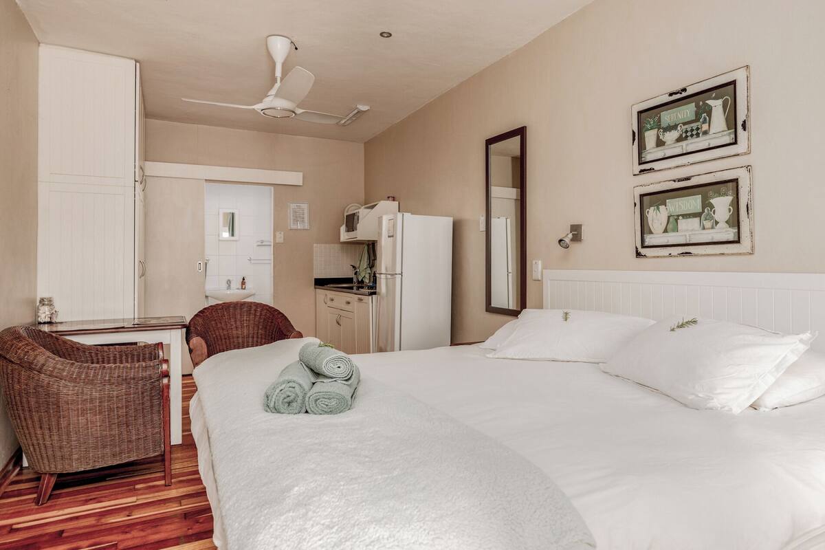 A hotel room with a bed, a chair, a desk, a mirror, and a ceiling fan.