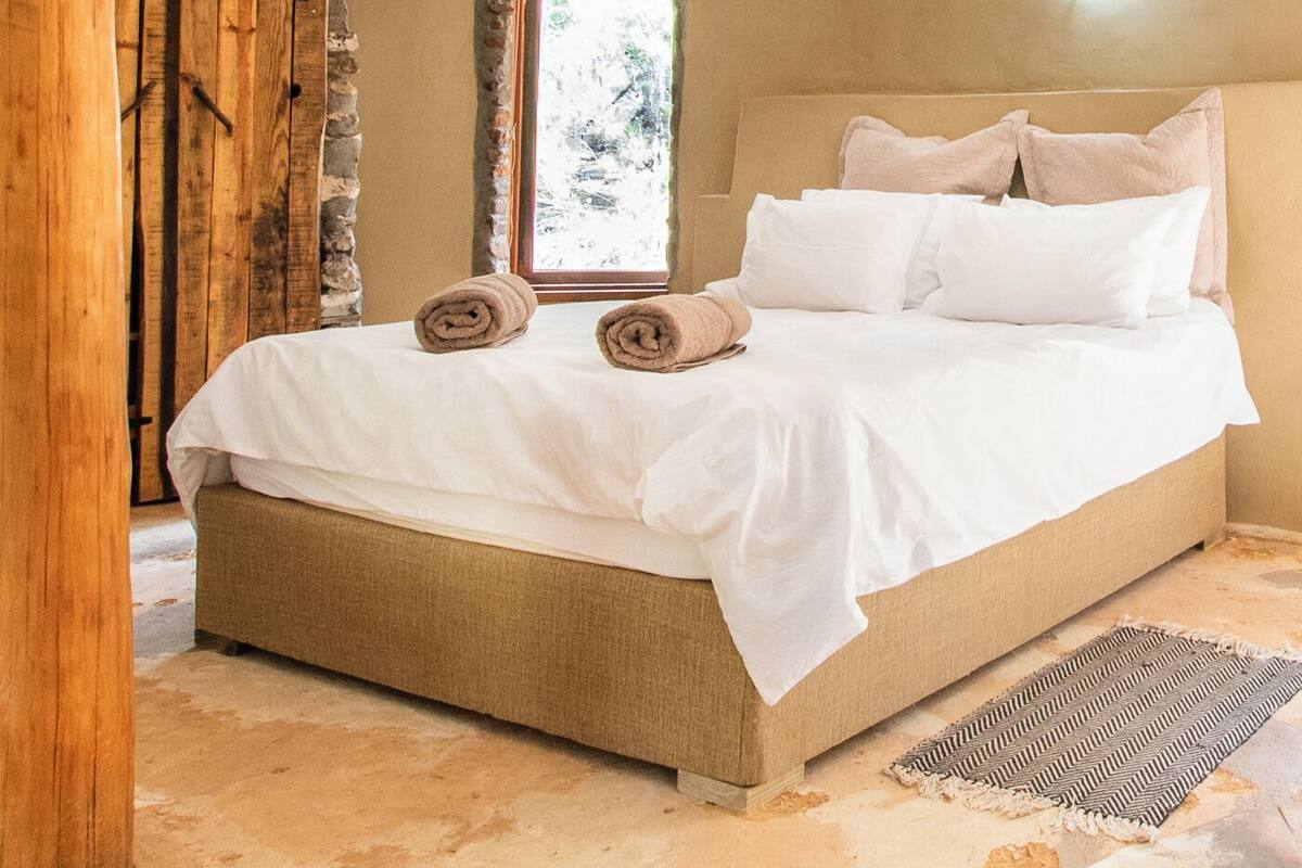 A bedroom with a bed, a window, a wooden door, and a stone wall.