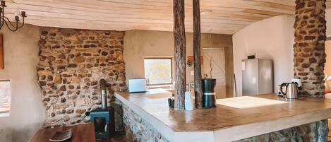 Una cocina rústica con una isla de piedra, vigas de madera en el techo y una pared de piedra.