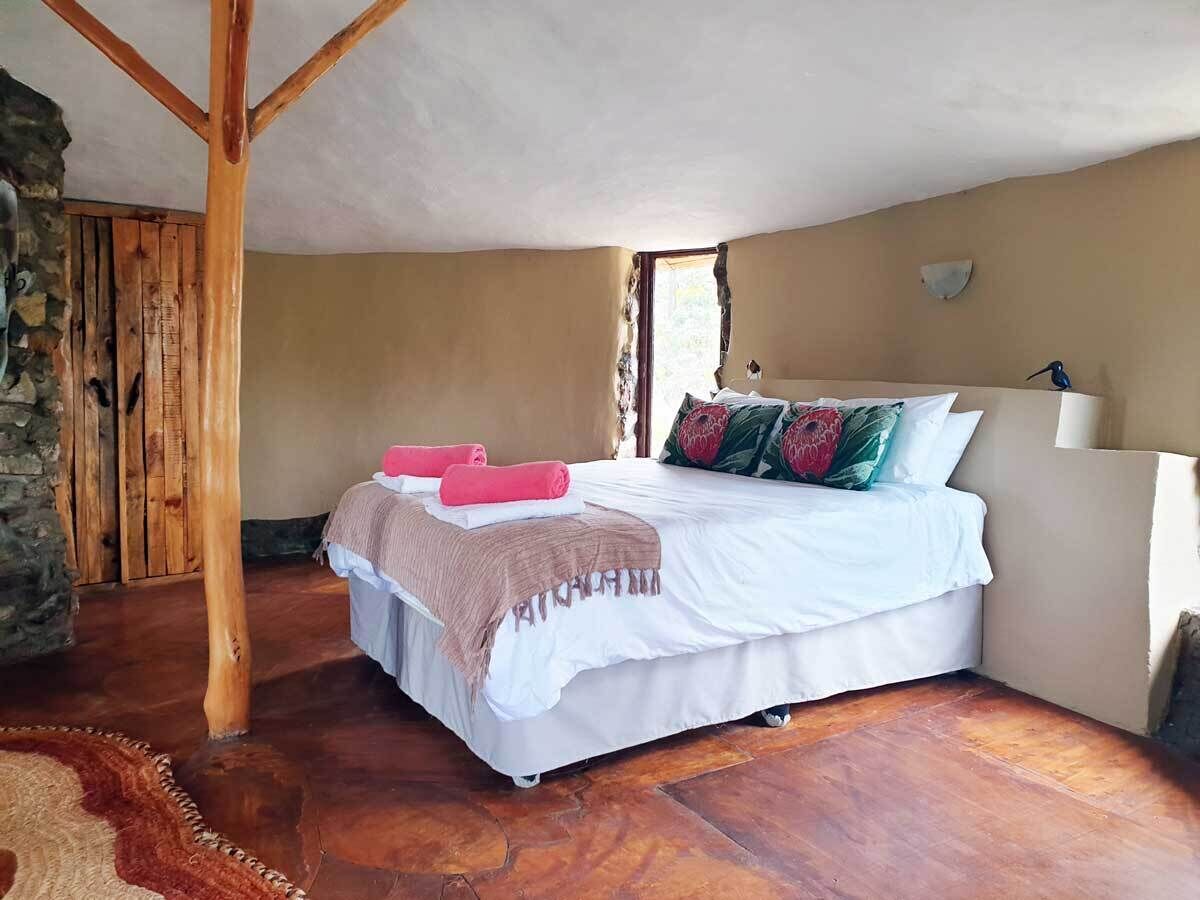 A bedroom with a bed, wooden floor, stone wall, and a window.