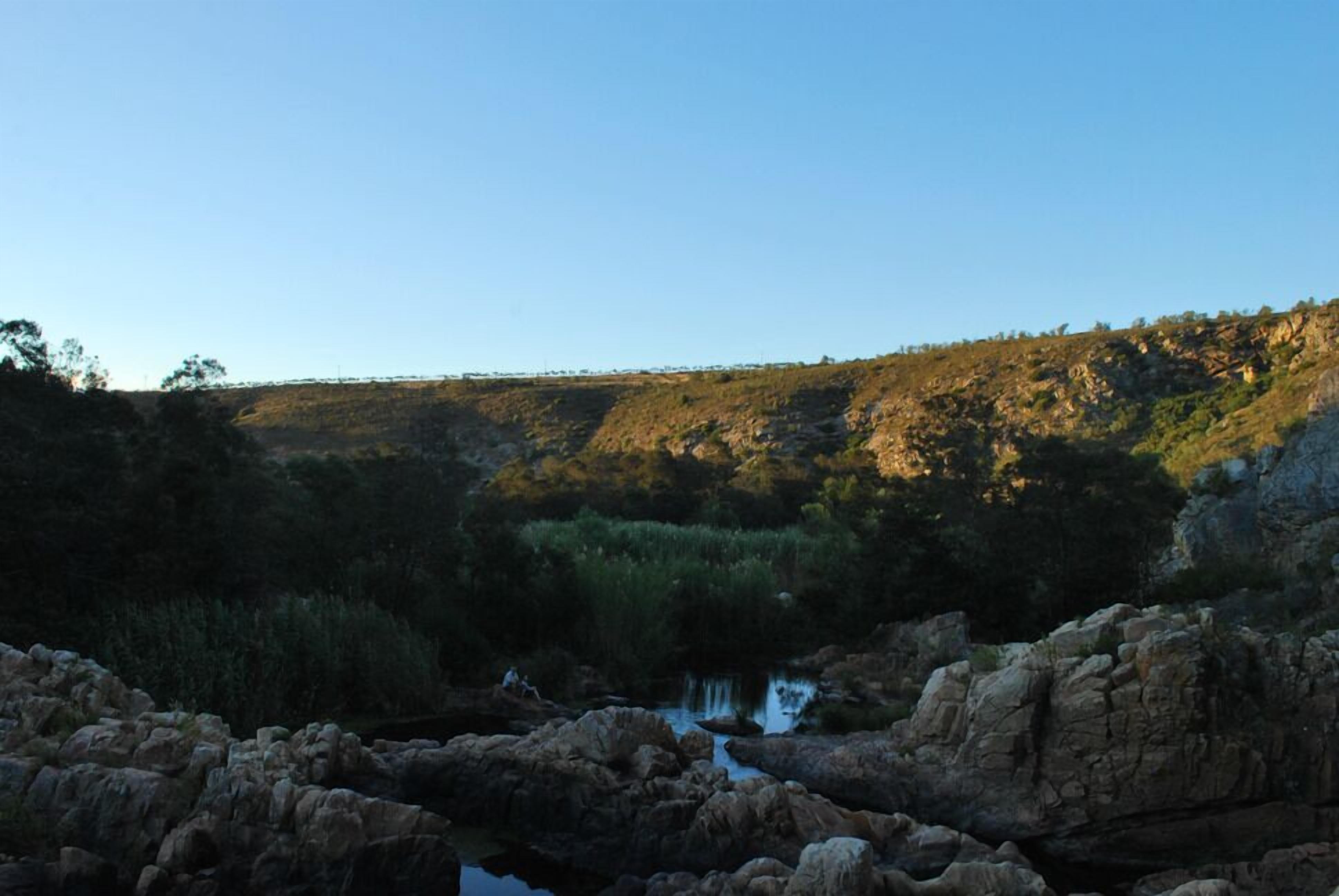 Paisaje natural con terreno rocoso, una pequeña masa de agua y cielo despejado.