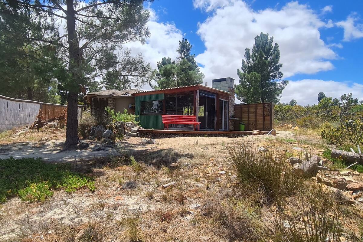 A rustic cabin with a wooden deck, surrounded by natural vegetation and trees.