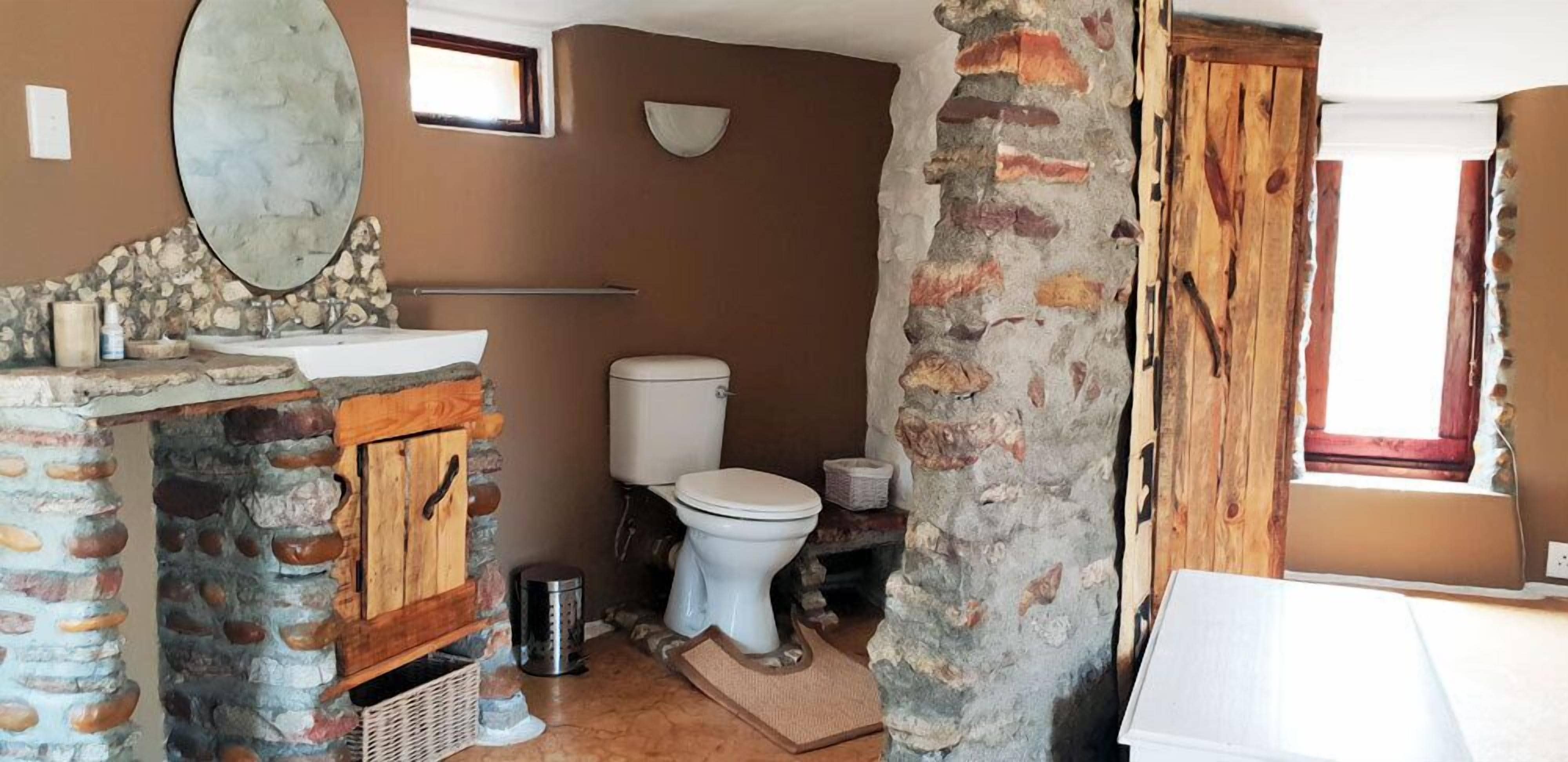 A rustic bathroom with a stone sink, a white toilet, and a large mirror.