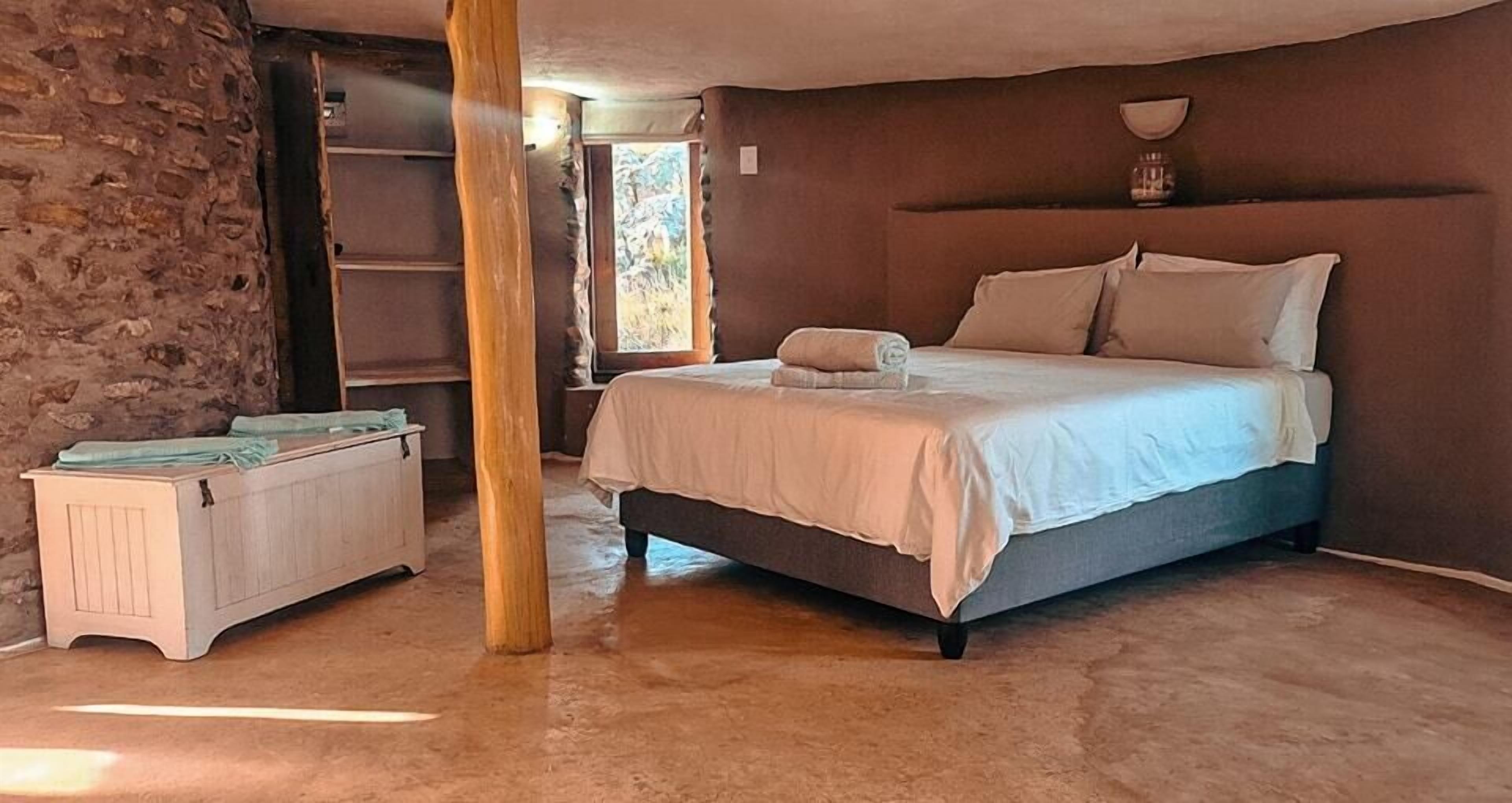 A bedroom with a bed, a wooden bench, and a stone wall.