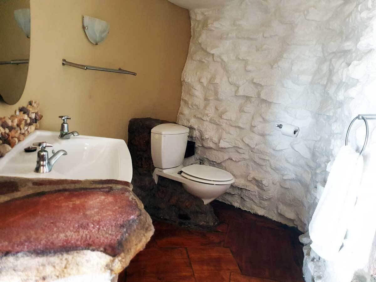 Un baño con lavamanos blanco, inodoro y pared de piedra.