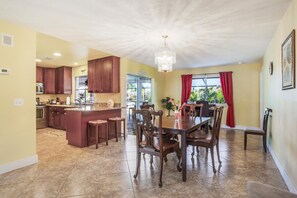 Enjoy meals in the dining area with a central island and bar stools, surrounded by a large chandelier and windows with a view.