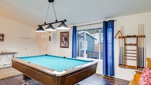 A pool table in a room with a window, a rack for pool cues, and a door. - Sea Break - Ocean view with Hot tub (Yachats)