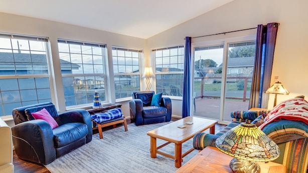A spacious living room with a large window, a wooden coffee table, and comfortable seating. - Sea Break - Ocean view with Hot tub (Yachats)