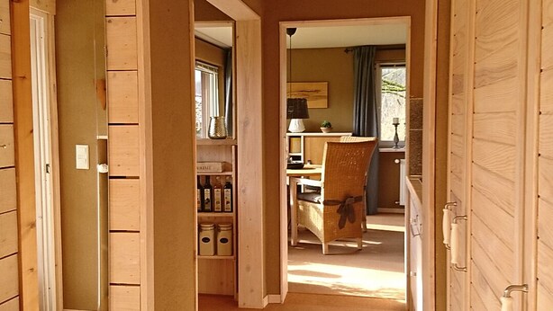 A hallway with wooden walls and a carpeted floor, leading to a dining area with a table and chairs. - Holiday house complex Hilkenberg house 2, in the middle of nature - romantic and quiet (Bodenfelde)