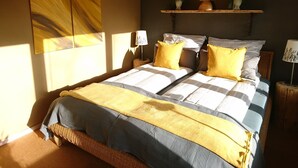 A bedroom with two beds, a shelf with decorative items, and a large abstract painting on the wall. - Holiday house complex Hilkenberg house 2, in the middle of nature - romantic and quiet (Bodenfelde)