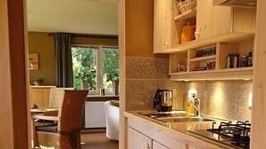 A modern kitchen with wooden cabinets, a built-in oven, and a window overlooking a garden. - Holiday house complex Hilkenberg house 2, in the middle of nature - romantic and quiet (Bodenfelde)