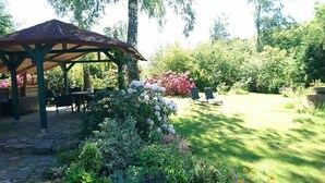 A gazebo with a tiled roof, surrounded by lush greenery and flowering plants. - Holiday house complex Hilkenberg house 2, in the middle of nature - romantic and quiet (Bodenfelde)