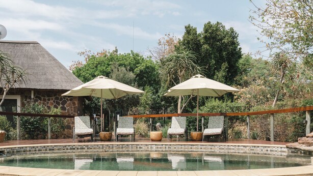 A pool area with lounge chairs and umbrellas, surrounded by stone walls and greenery. - Buccara Waterberg - Molapo (Lephalale)