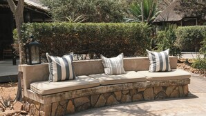 A stone bench with cushions and a lantern, surrounded by greenery and a thatched-roof building. - Buccara Waterberg - Molapo (Lephalale)