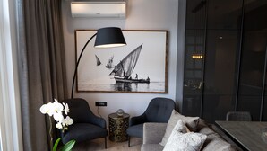 En moderne stue med en grå sofa, to lænestole, et sofabord og et stort sort-hvidt billede af en sejlbåd.