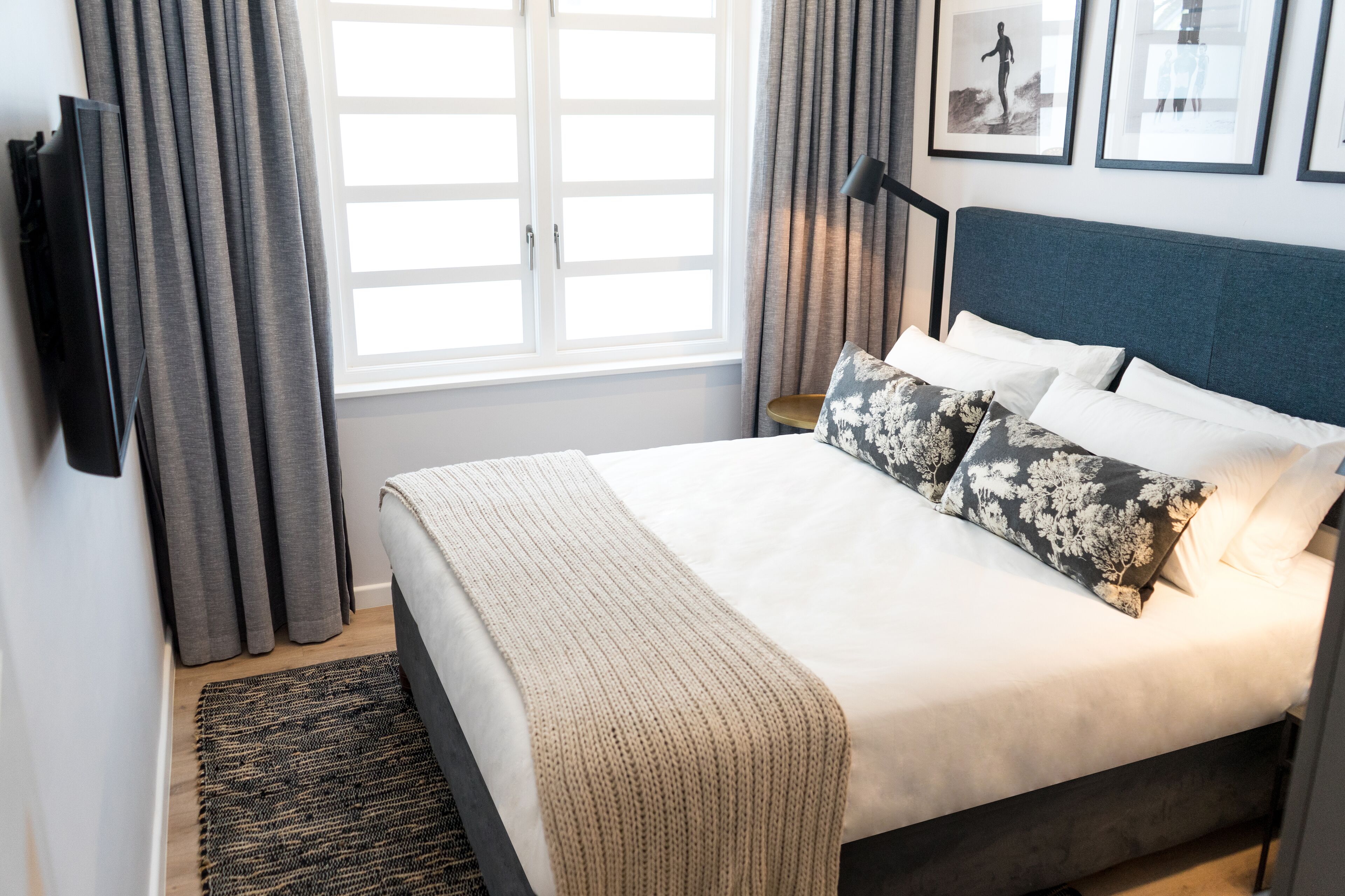 A neatly made bed with a beige blanket, grey curtains, and a framed picture on the wall.