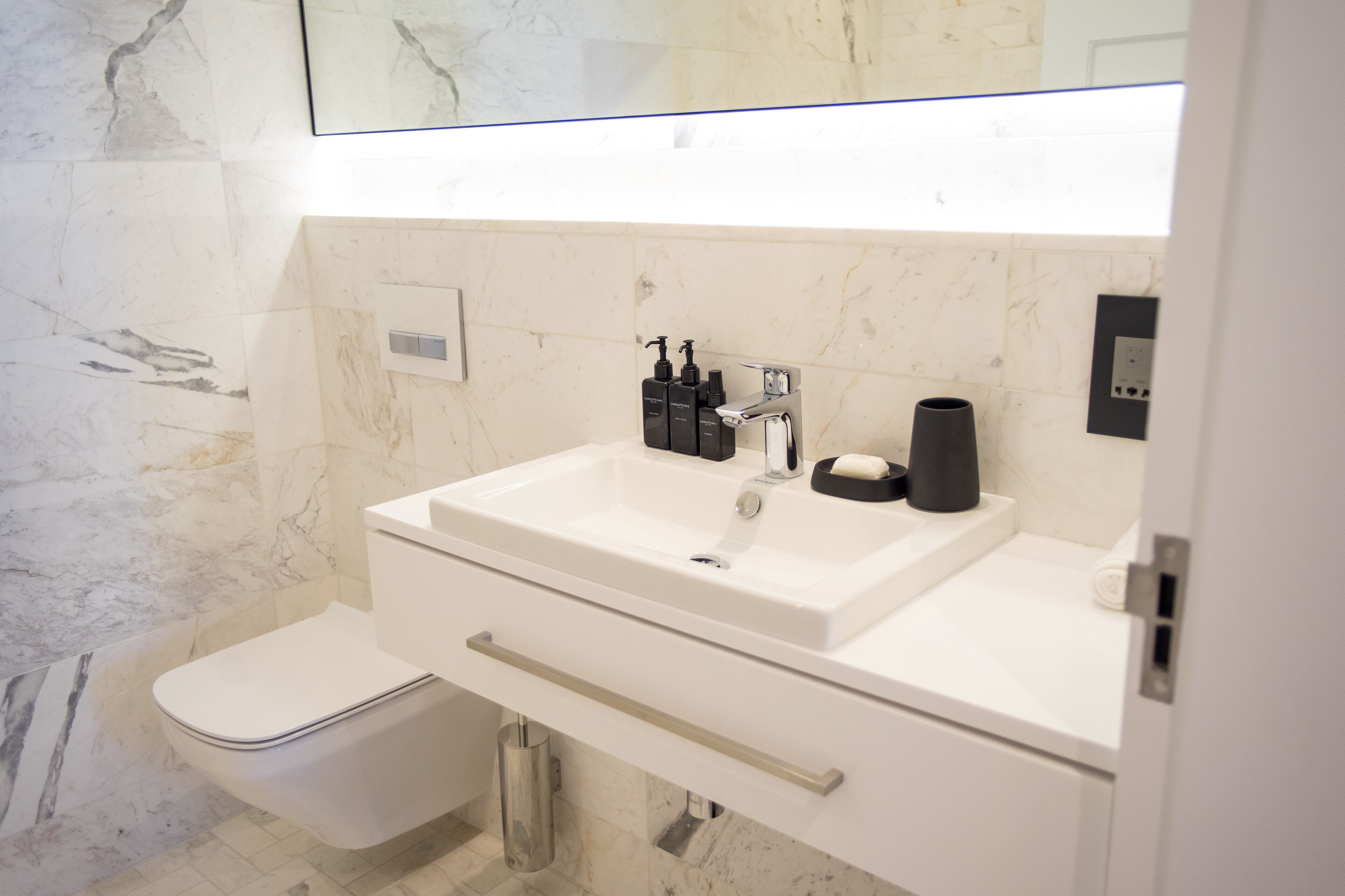 Une salle de bain moderne avec un lavabo blanc, des toilettes et un mur en marbre.