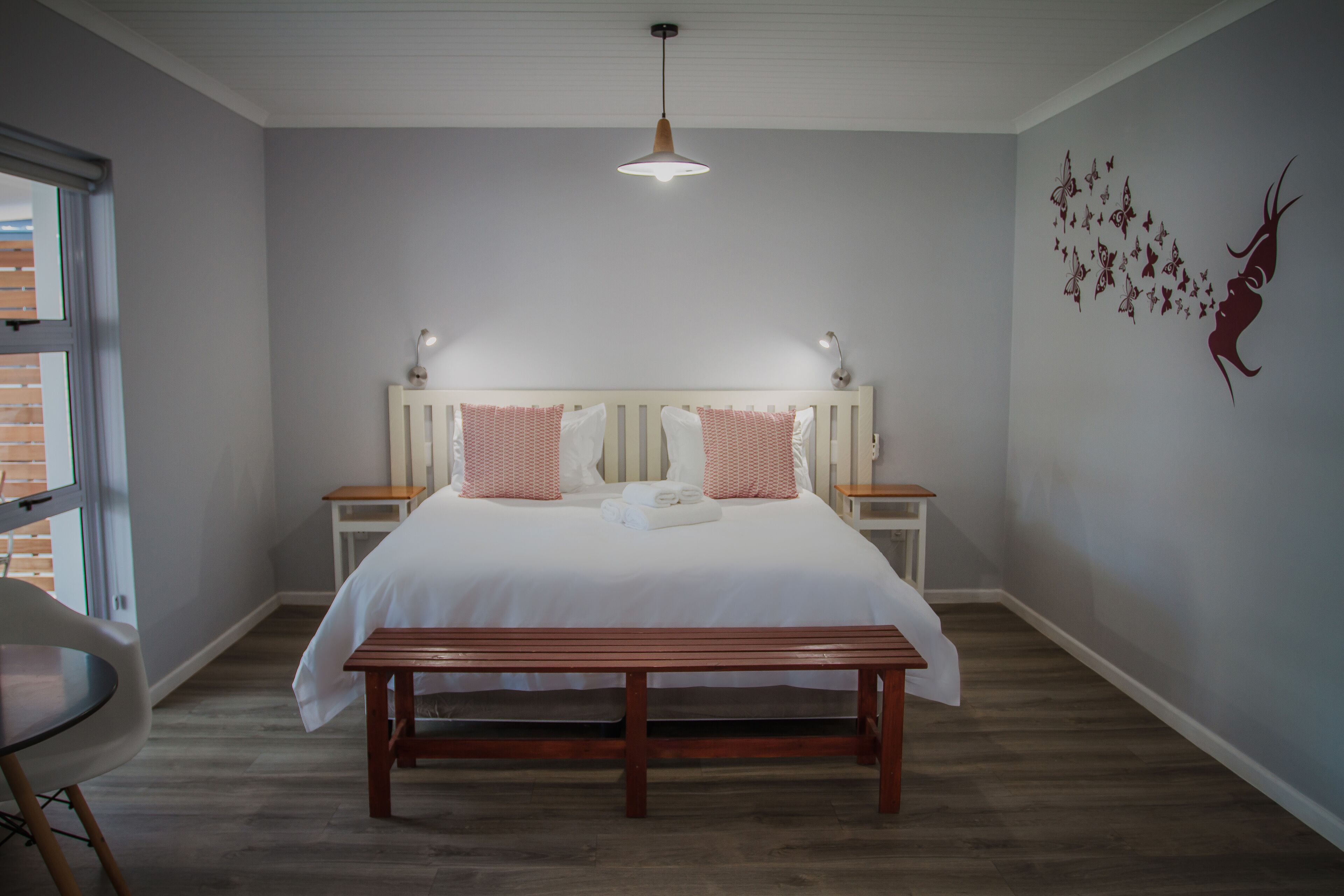 A bedroom with a large bed, bedside tables, a bench, and a wall with butterfly decals.