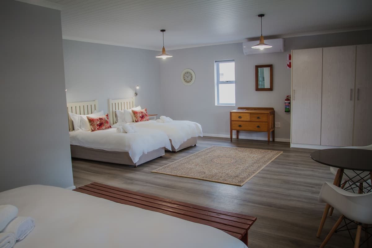 A modern bedroom with a large bed, bedside tables, a wooden bench, and a dining area with a table and chairs.