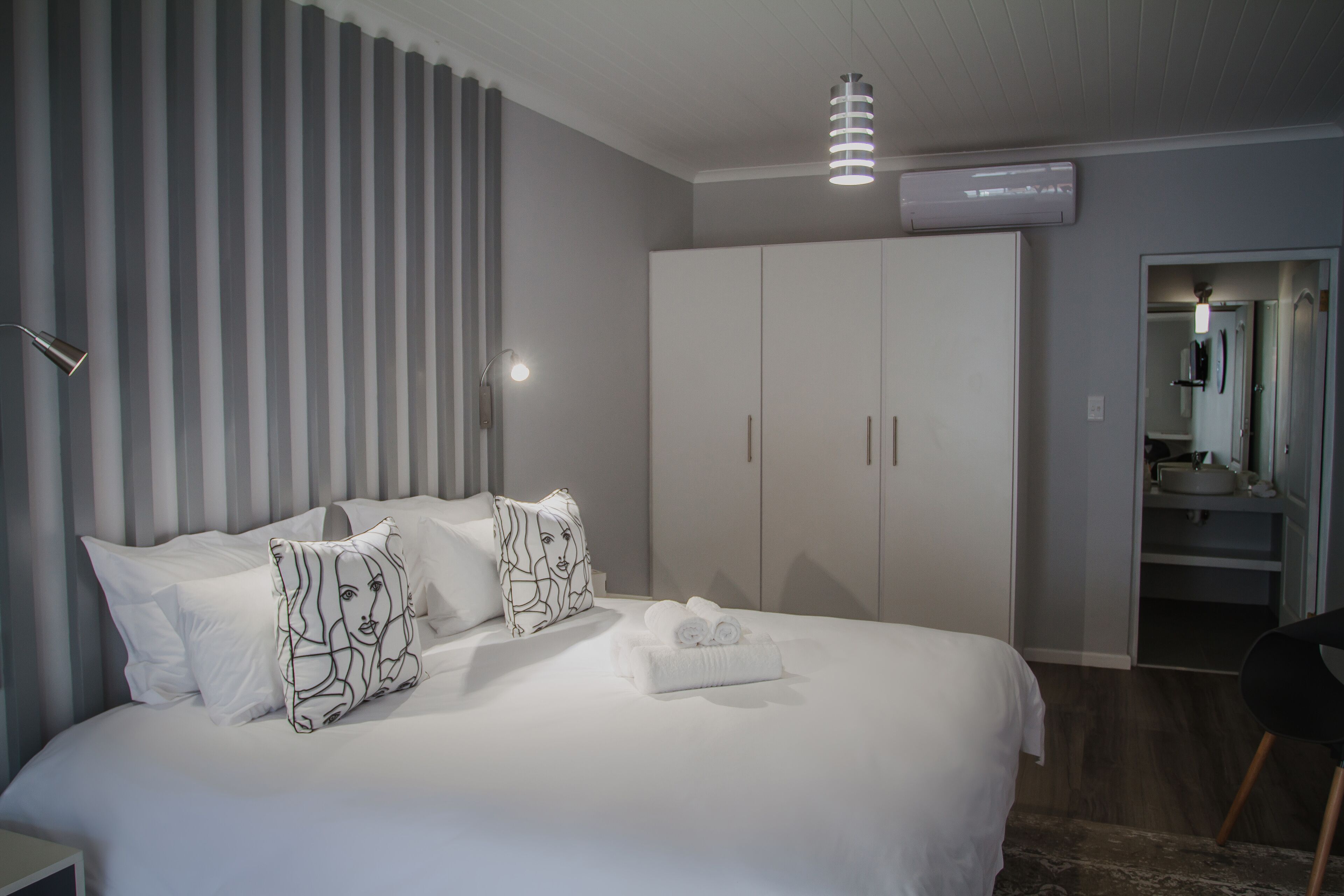 Habitación de hotel con una cama grande, ropa de cama blanca, un armario y un baño visible a través de una puerta abierta.