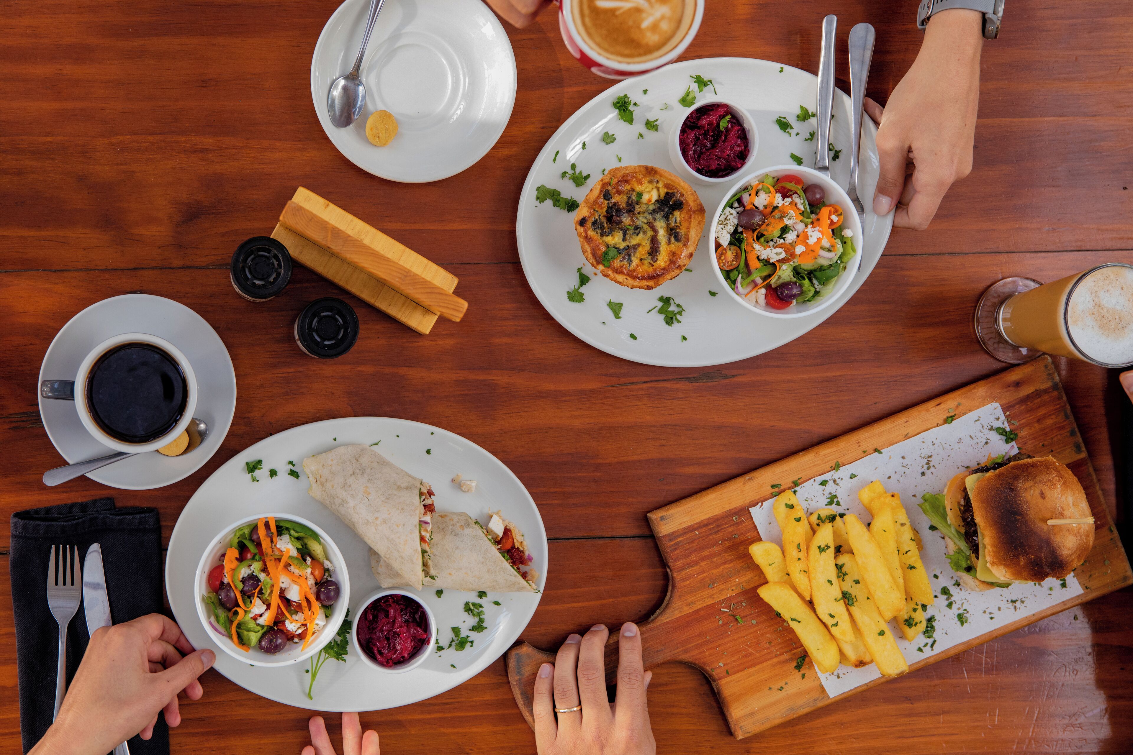 A wooden table with plates of food, a sandwich, and a cup of coffee.
