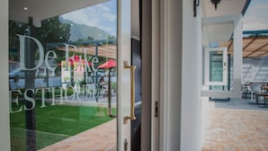 L’entrée d’un hôtel avec une porte en verre, un patio extérieur visible avec un sol en briques, et une vue sur une montagne en arrière-plan.