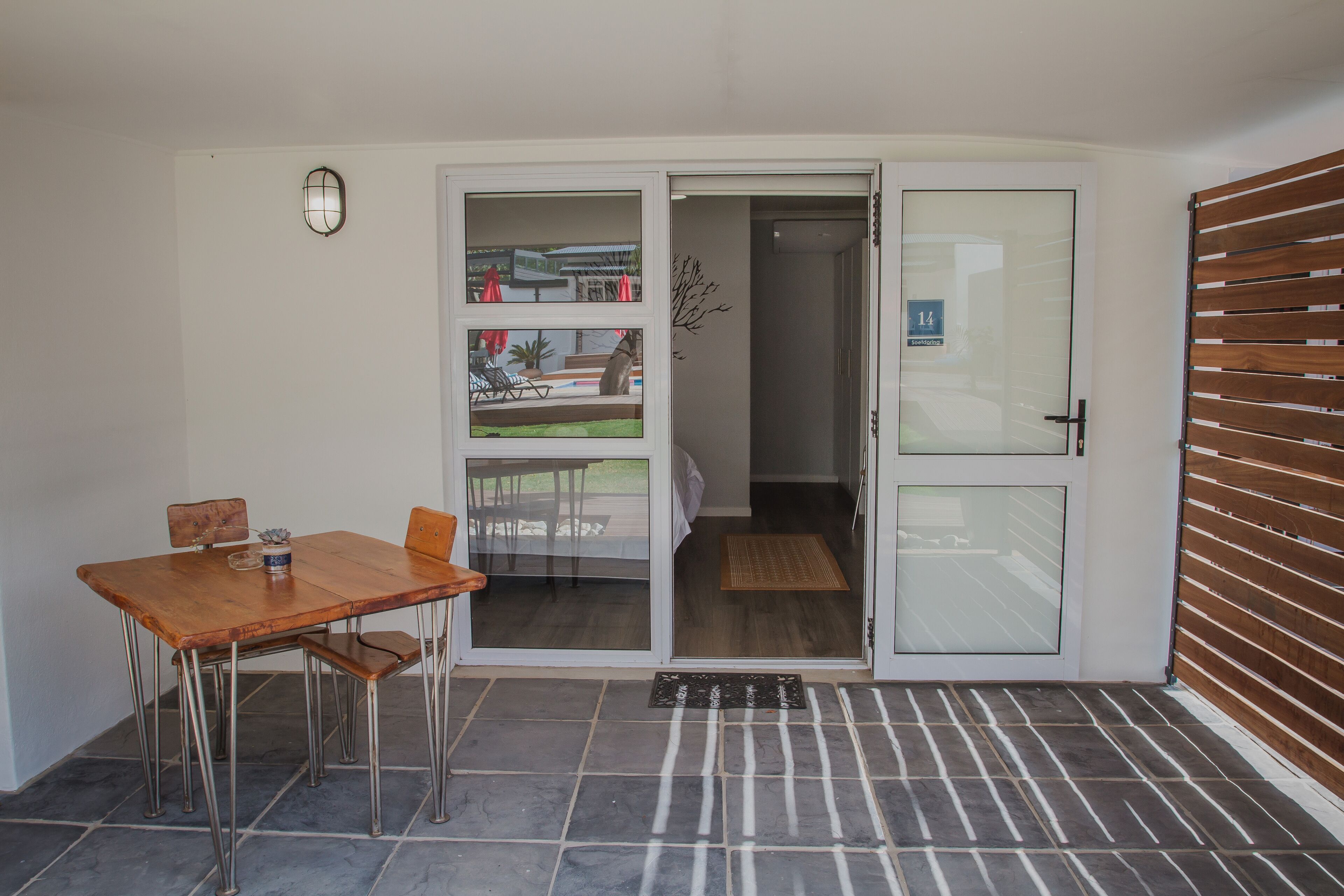 Ein kleiner Raum mit einem Holztisch und -stühlen, einer Schiebeglasdoor zum Balkon und einer Wand aus Holzlatten.