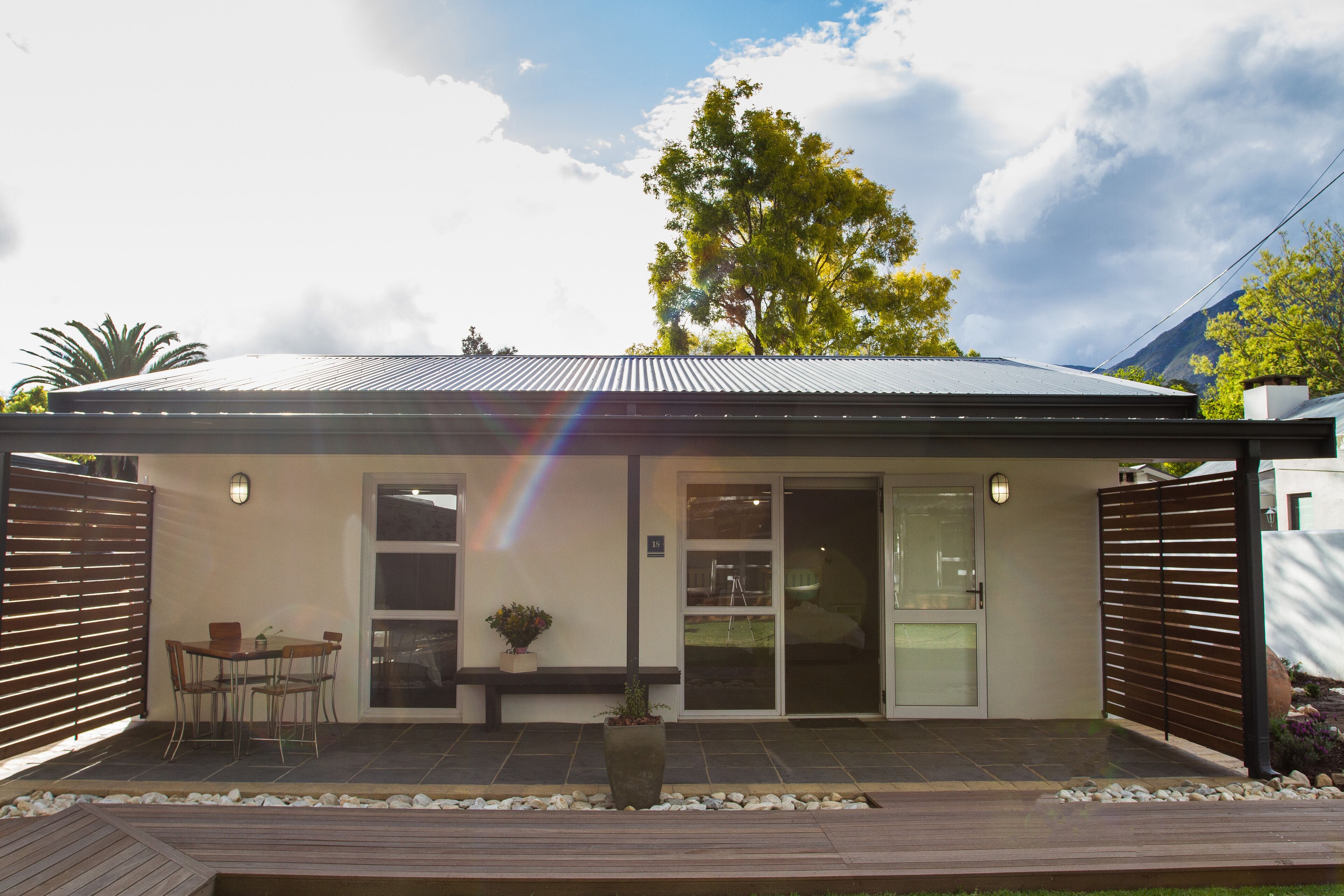 A modern house with a covered patio, a dining area, and a large tree in the background.
