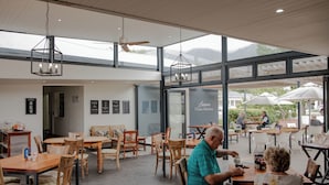 Un espace de restauration intérieur avec des tables et des chaises en bois, un ventilateur de plafond et de grandes fenêtres.