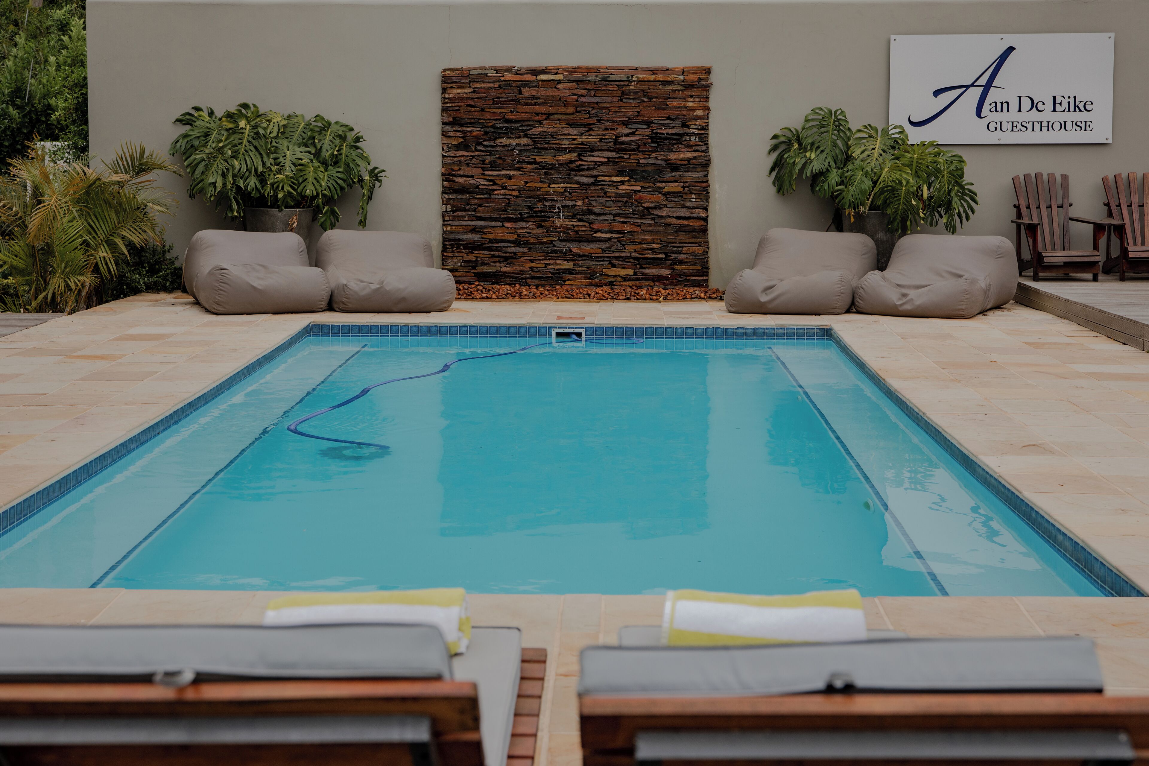 Un espace piscine avec des chaises longues, un mur en pierre et une pancarte indiquant « An De Eike Guesthouse ».