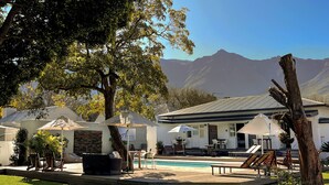 Un espace aménagé au bord de la piscine, avec des meubles d’extérieur, des parasols et une vue sur les montagnes.