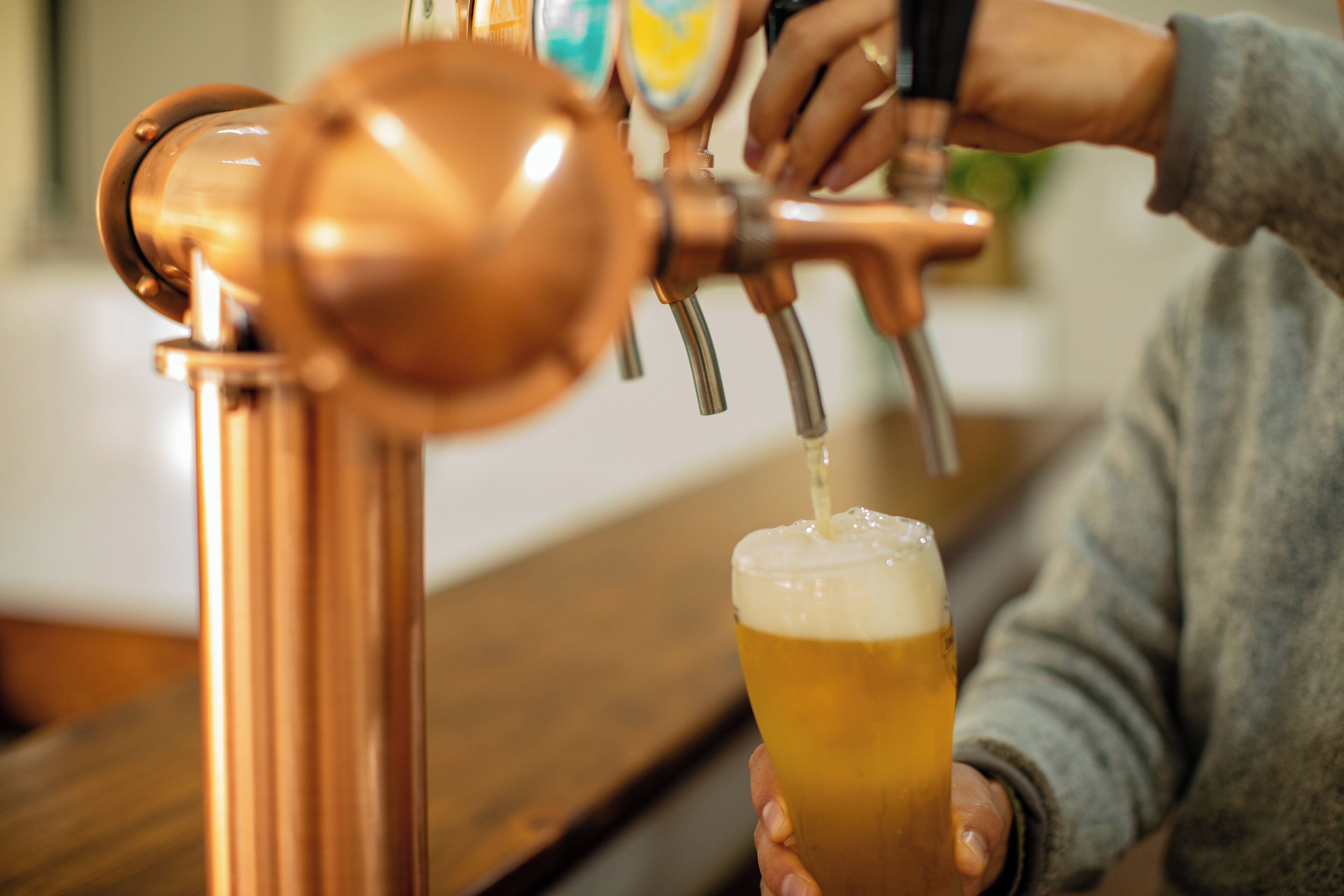 Una persona sirviendo cerveza desde un grifo de cobre en un vaso.