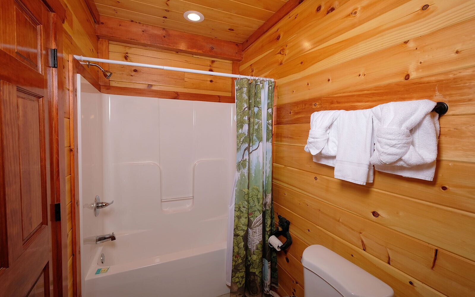 Baño de cabaña de madera con bañera, inodoro y cortina de ducha con estampado de árboles.