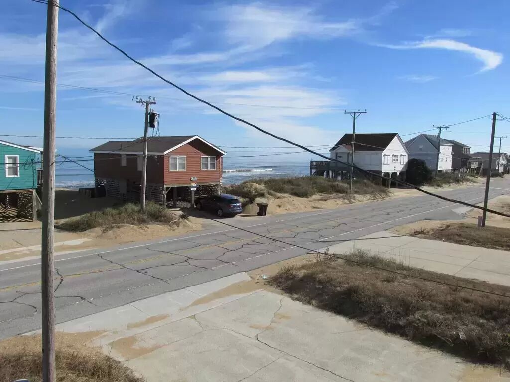 Una carretera costera con casas, un coche aparcado y cielo despejado.