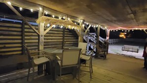 Ein Sitzbereich im Freien mit Tischen und Stühlen unter einer Holzkonstruktion, verziert mit Lichterketten.