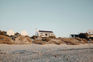 Et kystlandskab med en række hvide huse på en sandstrand, hvor et hus med solpaneler på taget er i fokus.