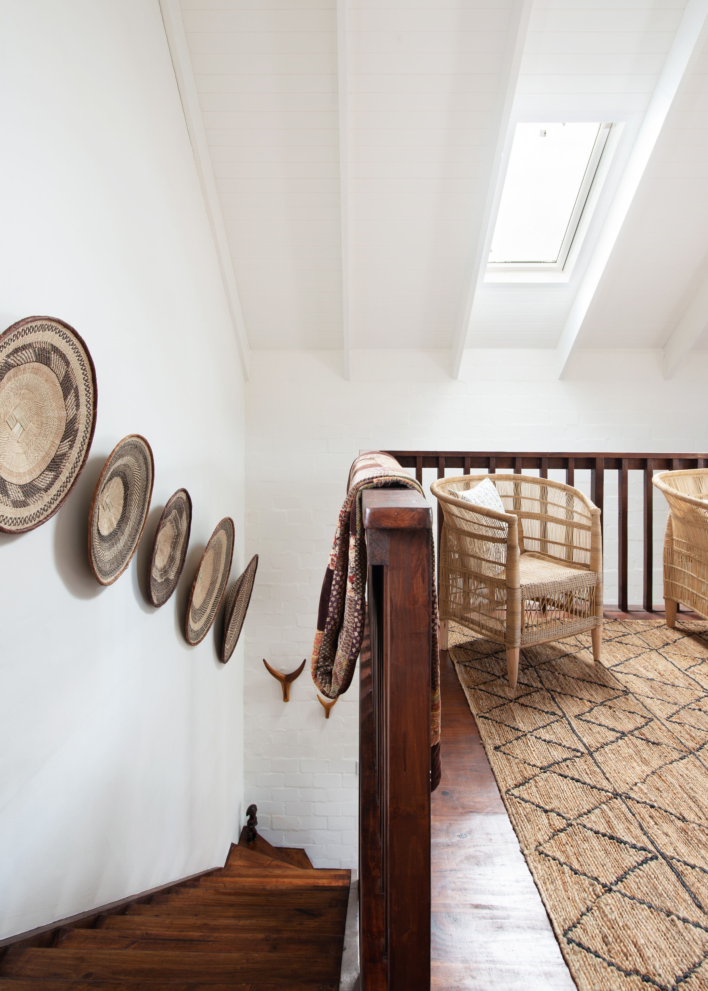 A staircase with a wooden handrail, a woven rug, and a wall with woven baskets.