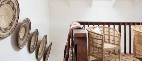 A staircase with a wooden handrail, a woven rug, and a wall with woven baskets.