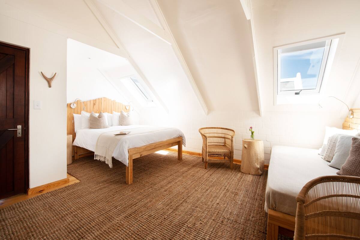 A bedroom with a sloped ceiling, a bed, a chair, and a small table.