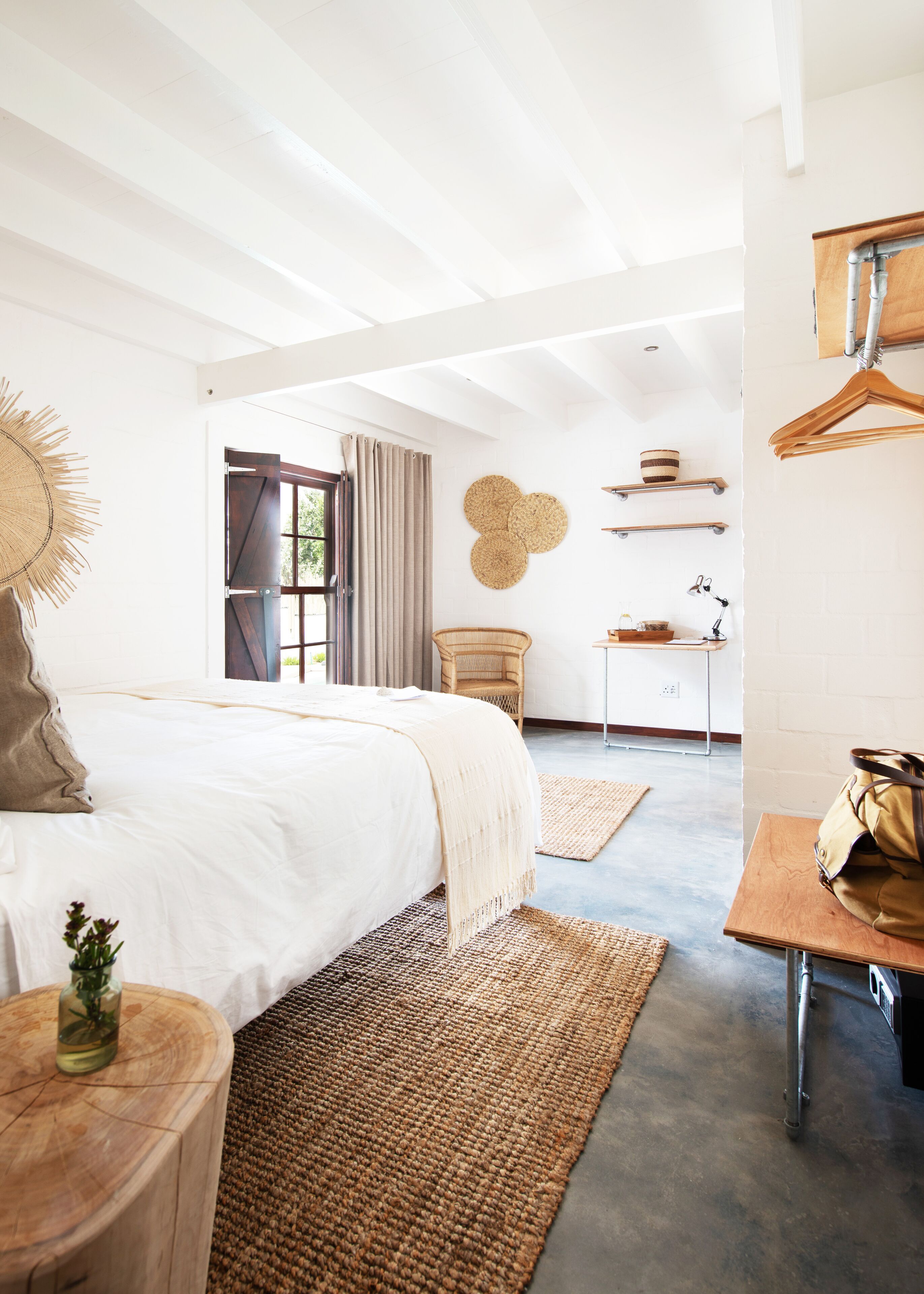 Un dormitorio moderno con una cama grande, una mesita de madera, una silla de mimbre y un escritorio con estantes.