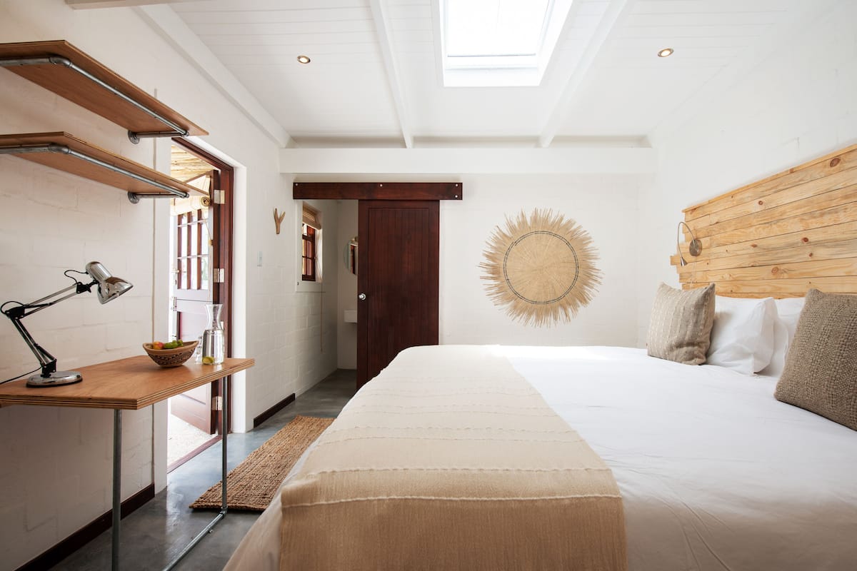 A bedroom with a bed, wooden headboard, a desk with a lamp, and a wall-mounted sunburst decoration.