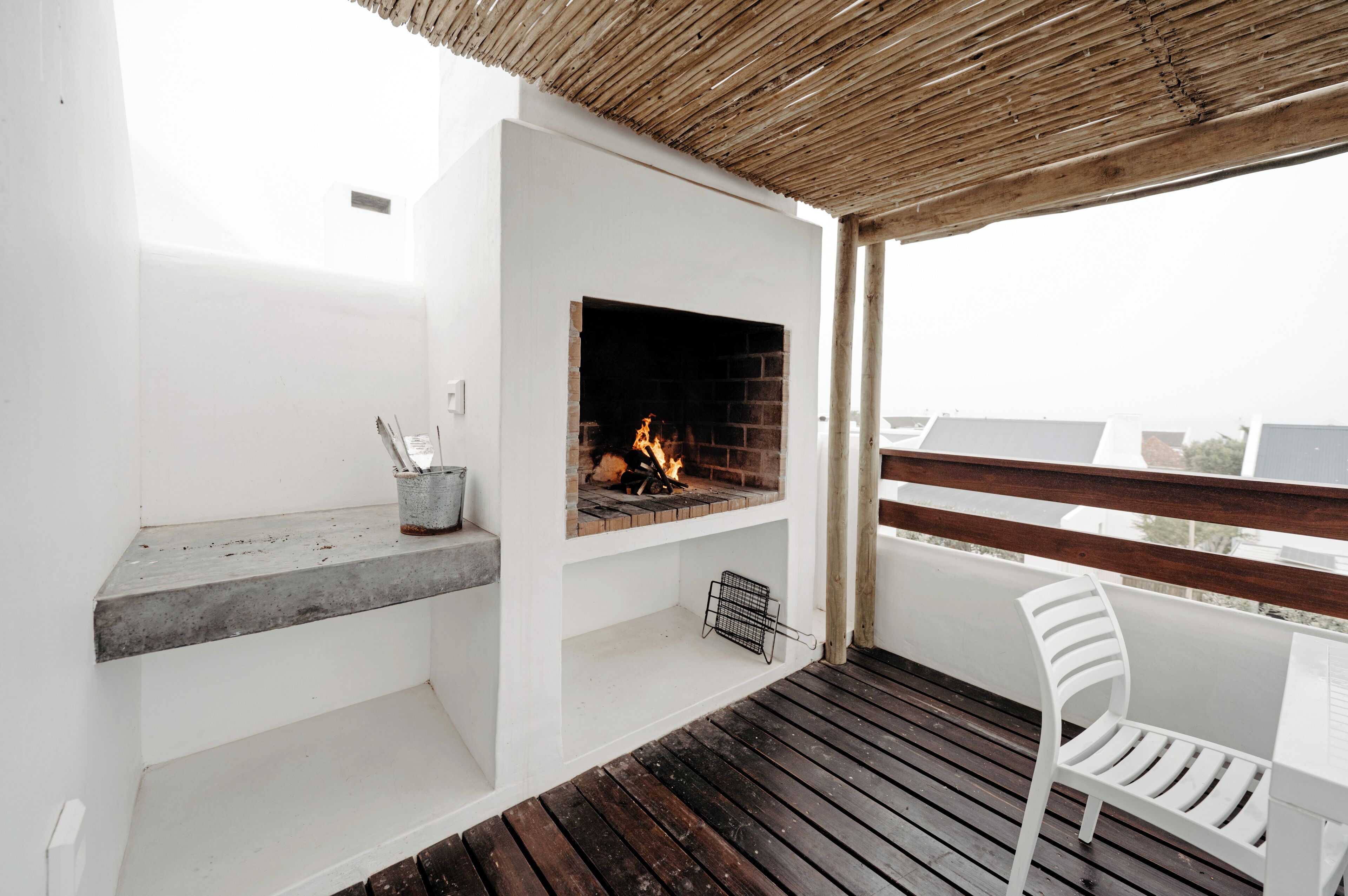 A balcony with a built-in fireplace, a white chair, and a wooden deck.